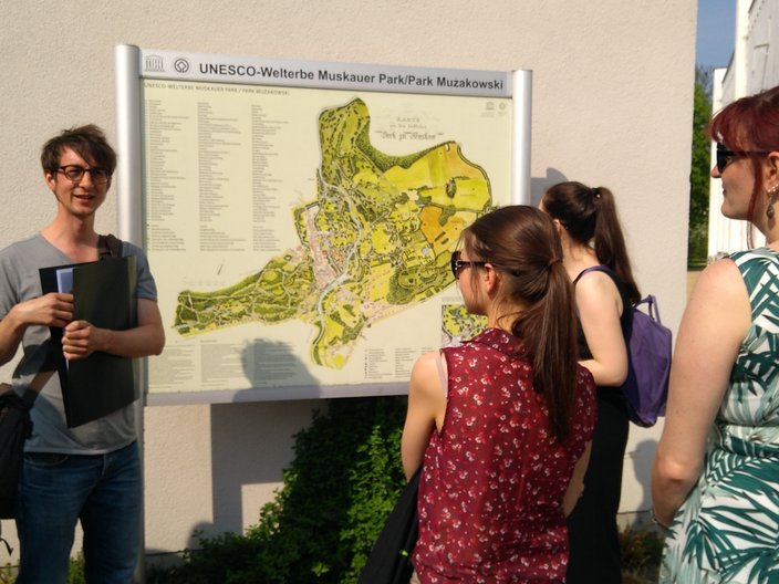 Vor einer Info-Tafeln informieren sich junge Menschen über das Welterbe Muskauer Park