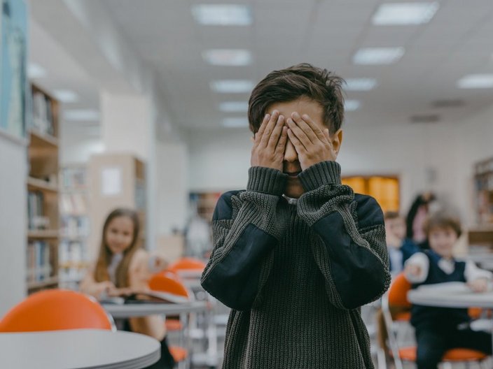 Ein Kind mit den Händen vor den Augen in einem Klassenzimmer.