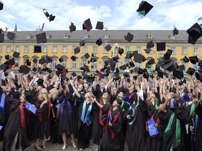 Absolventinnen und Absolventen werfen ihre Hüte vor der Universität Bonn in die Luft.