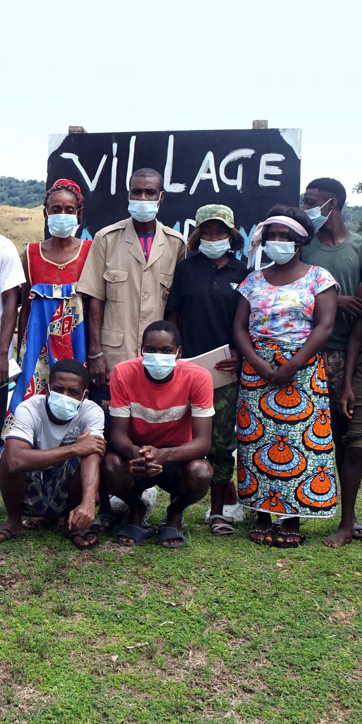 Gruppenfoto, auf dem Personen verschiedenen Alters zu sehen sind. Sie tragen eine Maske und blicken in die Kamera. 