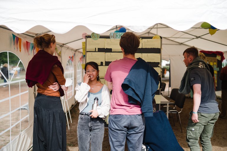 Vier Personen stehen vor einer Pinnwand unter einem Pavillon.