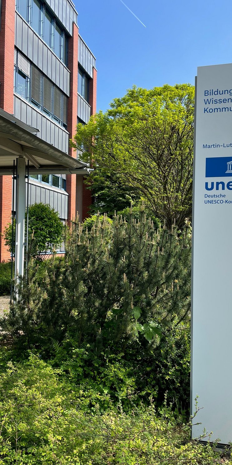 Weiße Stele mit blauem UNESCO-Logo und Adresse vor dem DUK-Gebäude