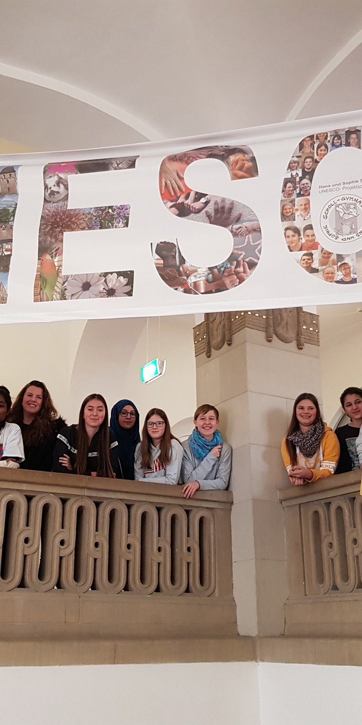 Schüler und Schülerinnen stehen im Treppenhaus der UPS Scholl Gymnasium in Ulm und über ihnen hängt ein Banner auf dem groß UNESCO steht.