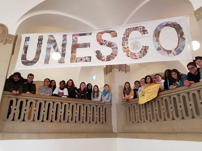 Schüler und Schülerinnen stehen im Treppenhaus der UPS Scholl Gymnasium in Ulm und über ihnen hängt ein Banner auf dem groß UNESCO steht.