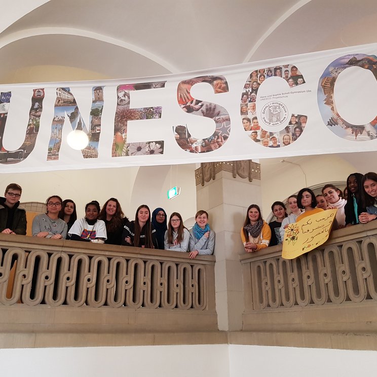 Schüler und Schülerinnen stehen im Treppenhaus der UPS Scholl Gymnasium in Ulm und über ihnen hängt ein Banner auf dem groß UNESCO steht.