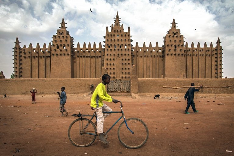 Ein Fahrradfahrer vor der beeindruckenden Kulisse eines Bauwerks der Alten Städte von Djenné 