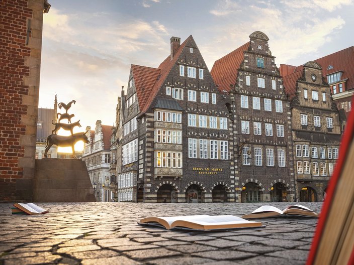 Die Bremer Stadtmusikanten neben dem Bremer Rathaus und aufgeschlagenen Büchern auf dem Kopfsteinpflaster