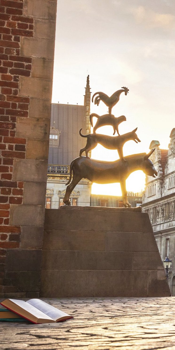 Die Bremer Stadtmusikanten neben dem Bremer Rathaus und aufgeschlagenen Büchern auf dem Kopfsteinpflaster