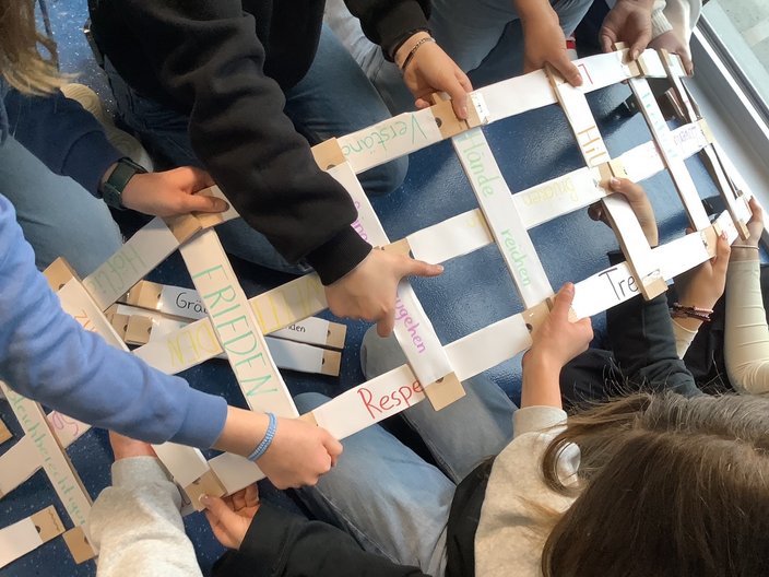 Schüler*innen halten eine selbstgebaute Brücke aus Holz.