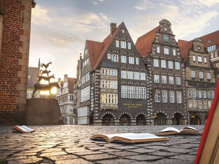 Die Bremer Stadtmusikanten neben dem Bremer Rathaus und aufgeschlagenen Büchern auf dem Kopfsteinpflaster