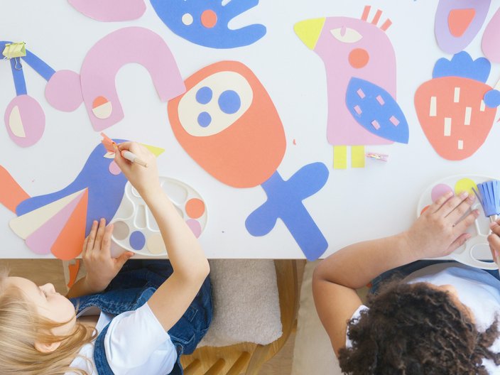 Zwei Mädchen im Kindergartenalter sitzen an einem Tisch und malen. Das Foto zeigt Sie aus der Vogelperspektive