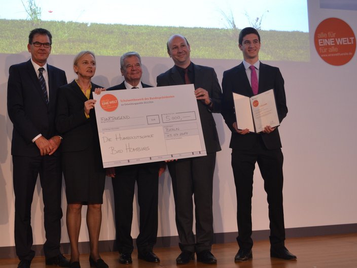 Vier Personen der Humboldtschule stehen neben dem damaligen Bundespräsidenten Joachim Gauck auf der Bühne und erhalten einen großen Check über 5.000 Euro im Rahmen des Schulwettbewerbs "alle für eine Welt für alle".