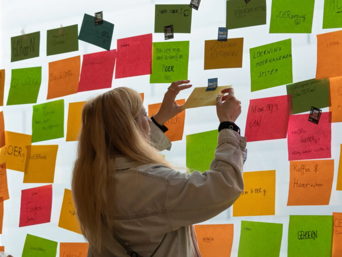 Eine Frau hängt ein Post-it an eine Wand. 