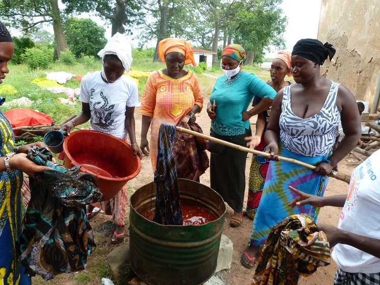 Frauen betreiben Batikkunst in Gambia. Sie tauchen Tücher in eine rote Flüssigkeit. 