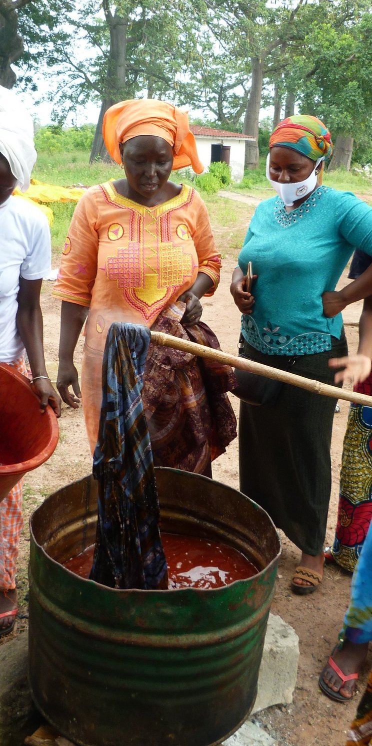 Frauen betreiben Batikkunst in Gambia. Sie tauchen Tücher in eine rote Flüssigkeit. 