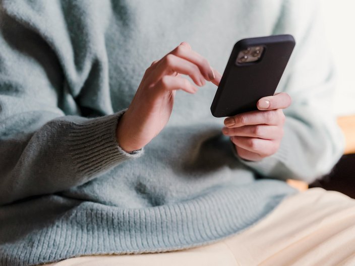 Blick auf eine Frau, die ein Smartphone in der Hand hält.